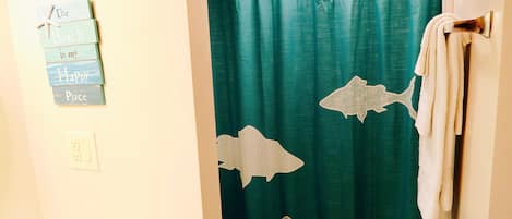 A bathroom with a teal shower curtain featuring shark designs, a towel rack, and a sign on the wall.