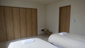 A hotel room with two beds, a wooden wardrobe, a small round table, and a door with circular cutouts. - Bliss & Bless Furano (Furano)