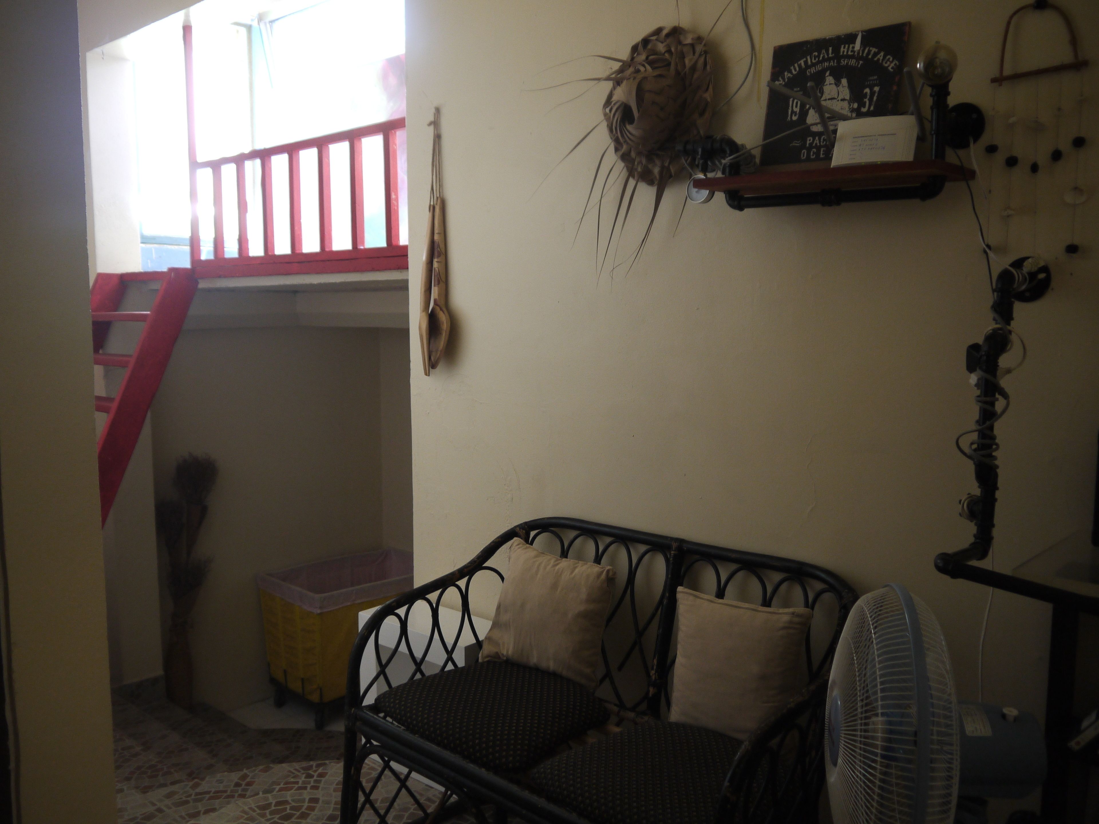 Una habitación con cama, ventilador, estante con un libro, escalera y un adorno en la pared.