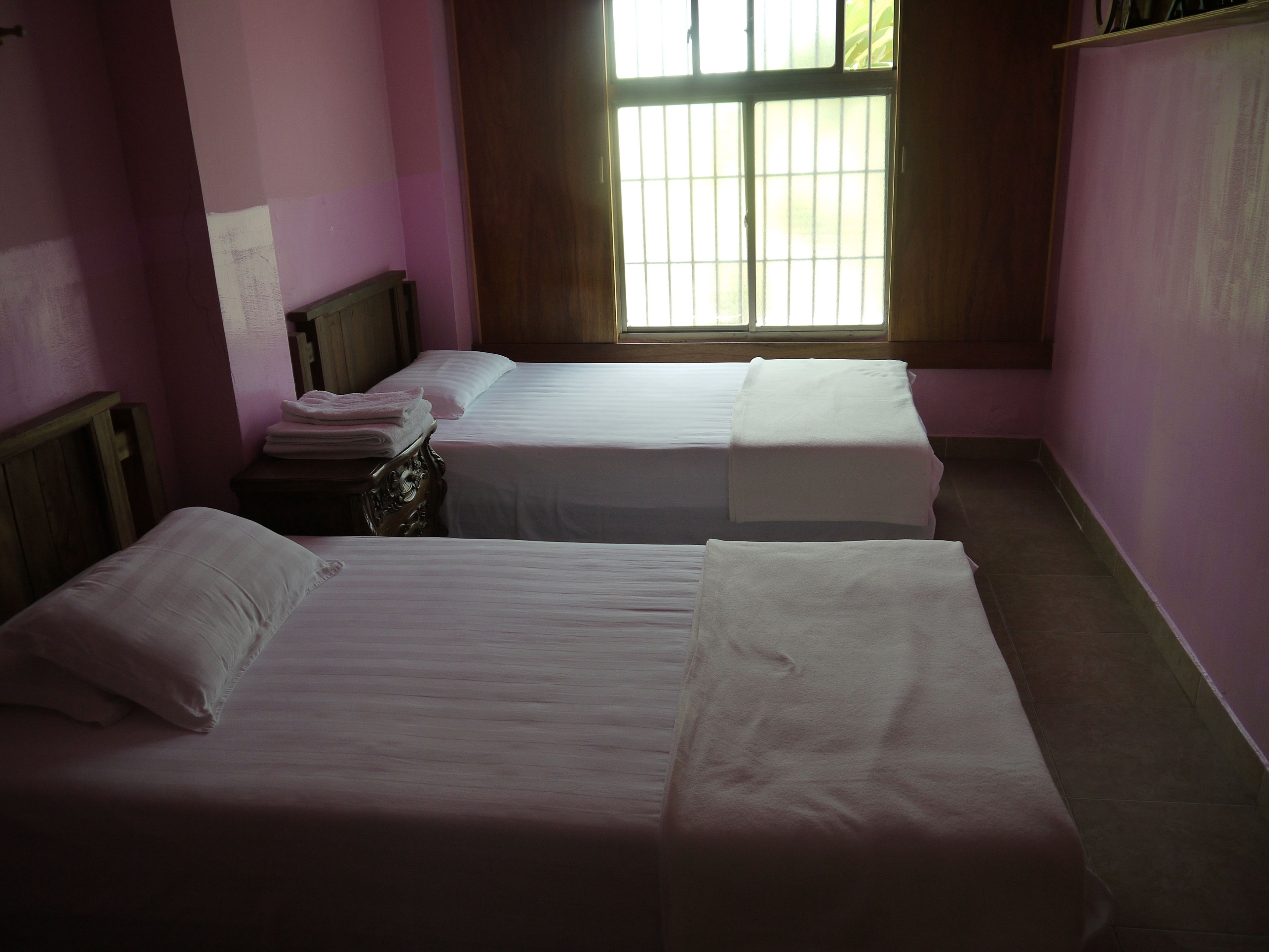 A room with two single beds, a nightstand, and a window with bars.