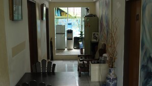 A dining area with a long table and chairs, a refrigerator, a water dispenser, and a vase with branches. - G.T. Guest House (Saipan)
