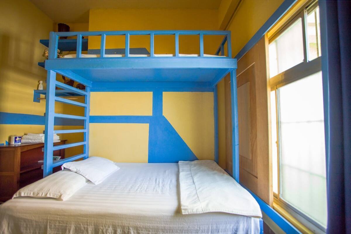 A bunk bed room with a window, a desk, and a chair.