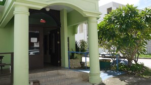 A building with a green facade, a covered entrance with steps, and a security camera. - G.T. Guest House (Saipan)
