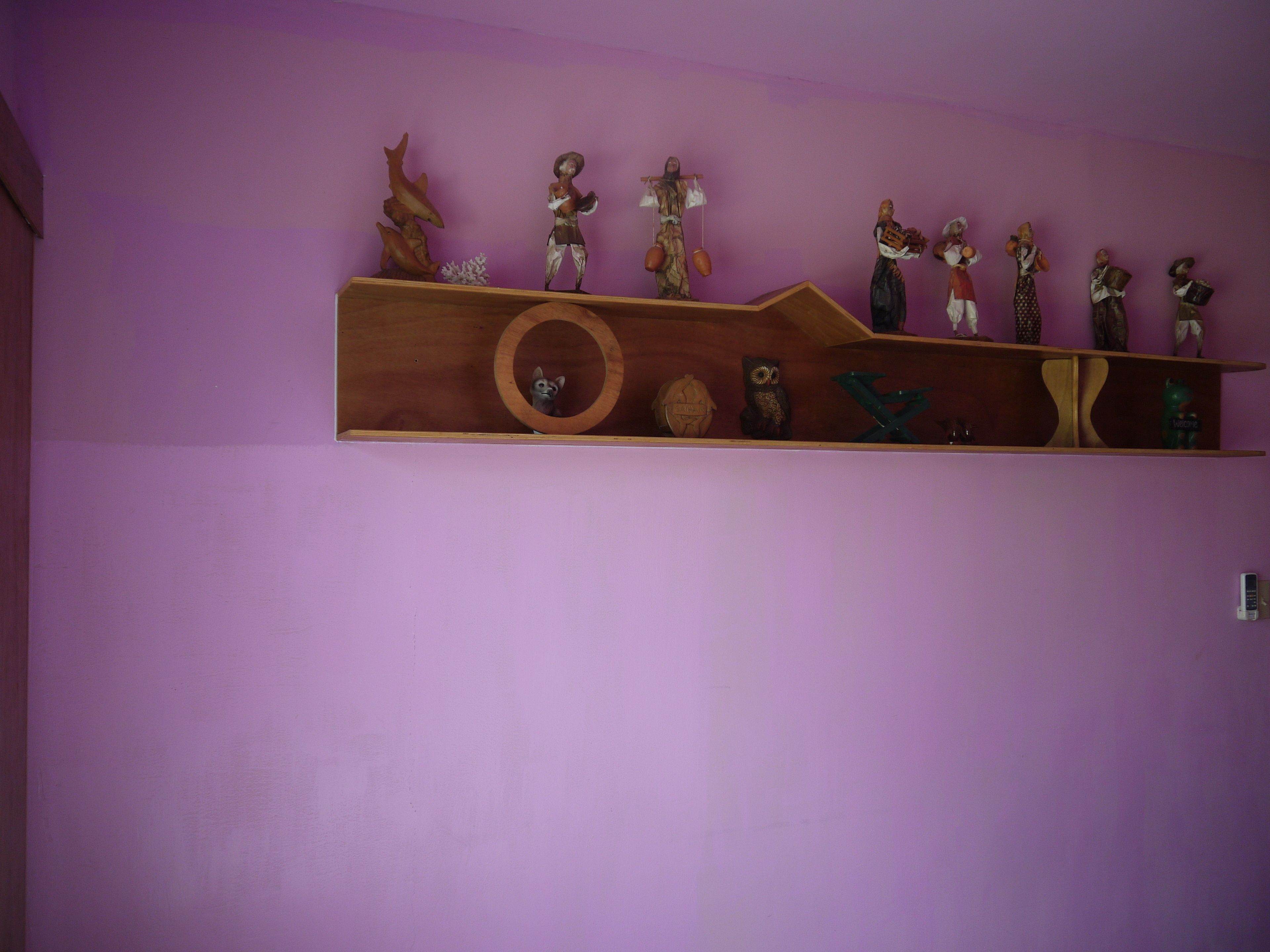 Una estant de fusta amb diverses figures i objectes decoratius davant d'una paret morada.