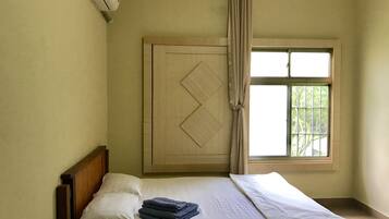 Un lit simple avec du linge de lit blanc, une tête de lit en bois et une fenêtre avec des rideaux.
