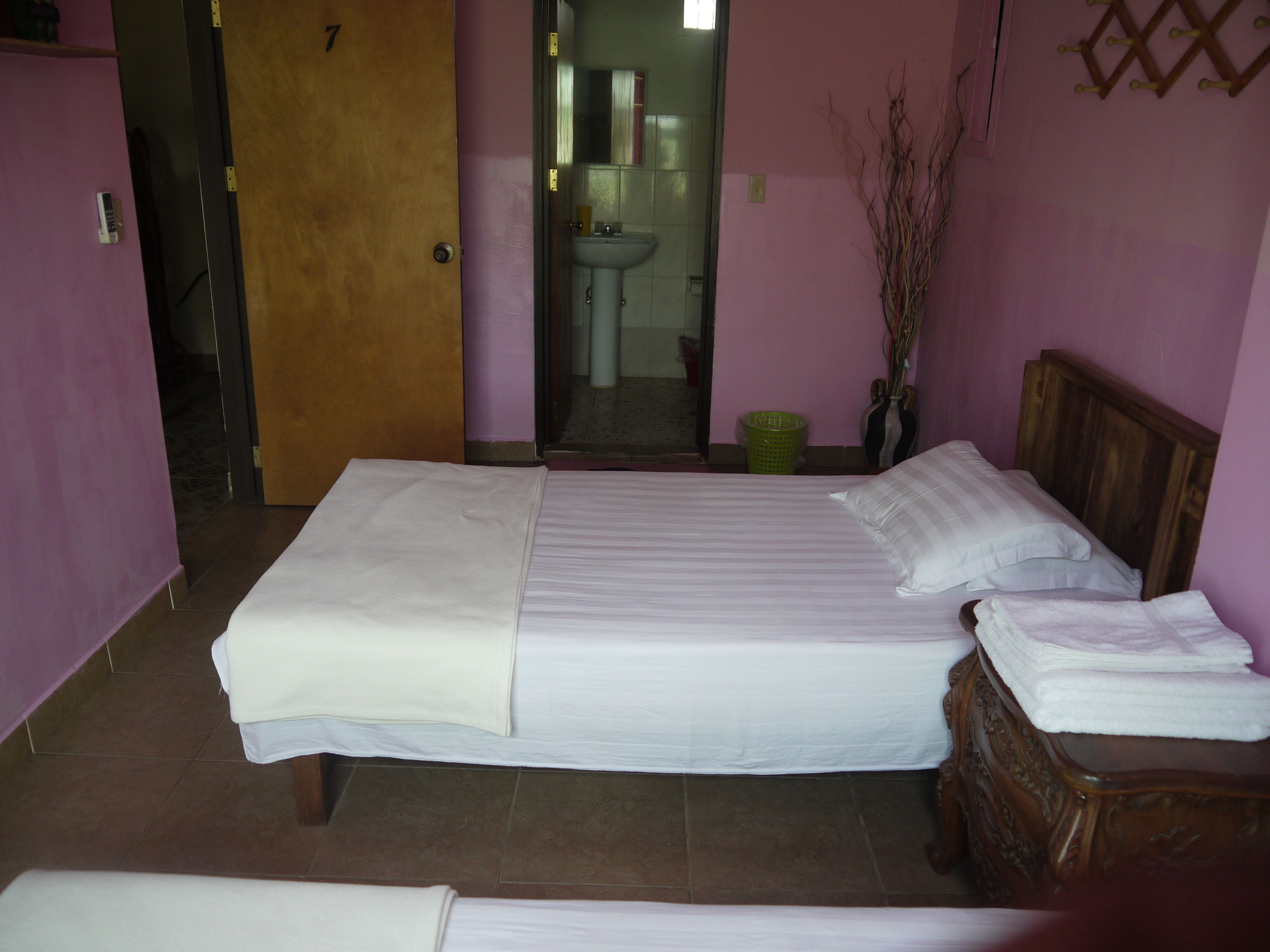 A room with a bed, a wooden headboard, a nightstand, a green trash bin, and a wall-mounted rack.