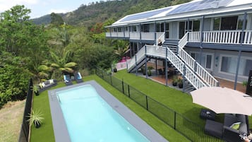 A pool with a surrounding deck, a covered outdoor seating area, and a building with solar panels.
