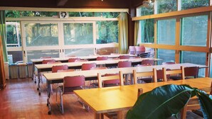 A classroom with wooden tables and chairs, large windows with curtains, and a ceiling fan. - Amanohashidate Youth Hostel (Miyazu)
