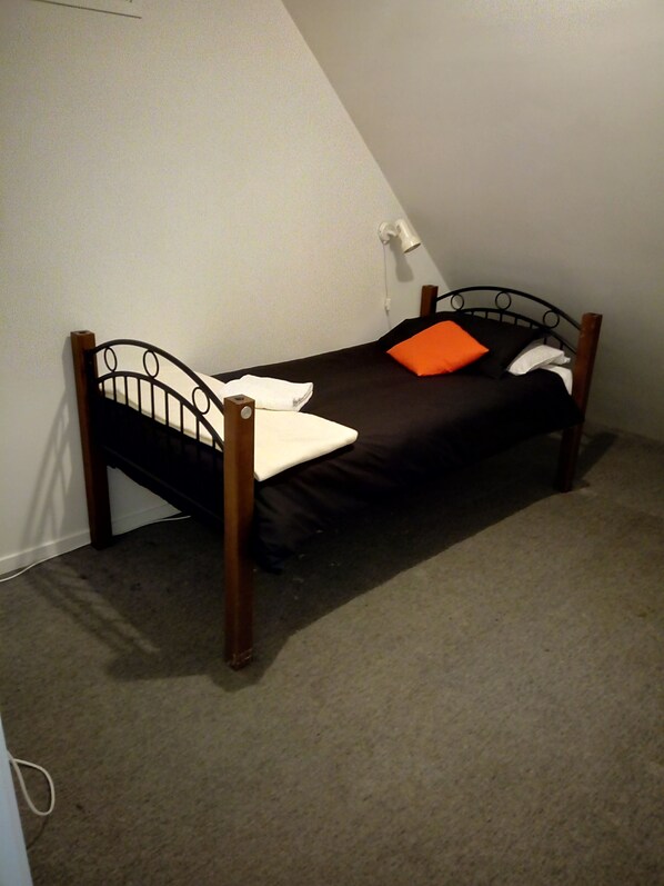 A small, single-bed room with a sloped ceiling, a bedside lamp, and a plain wall.