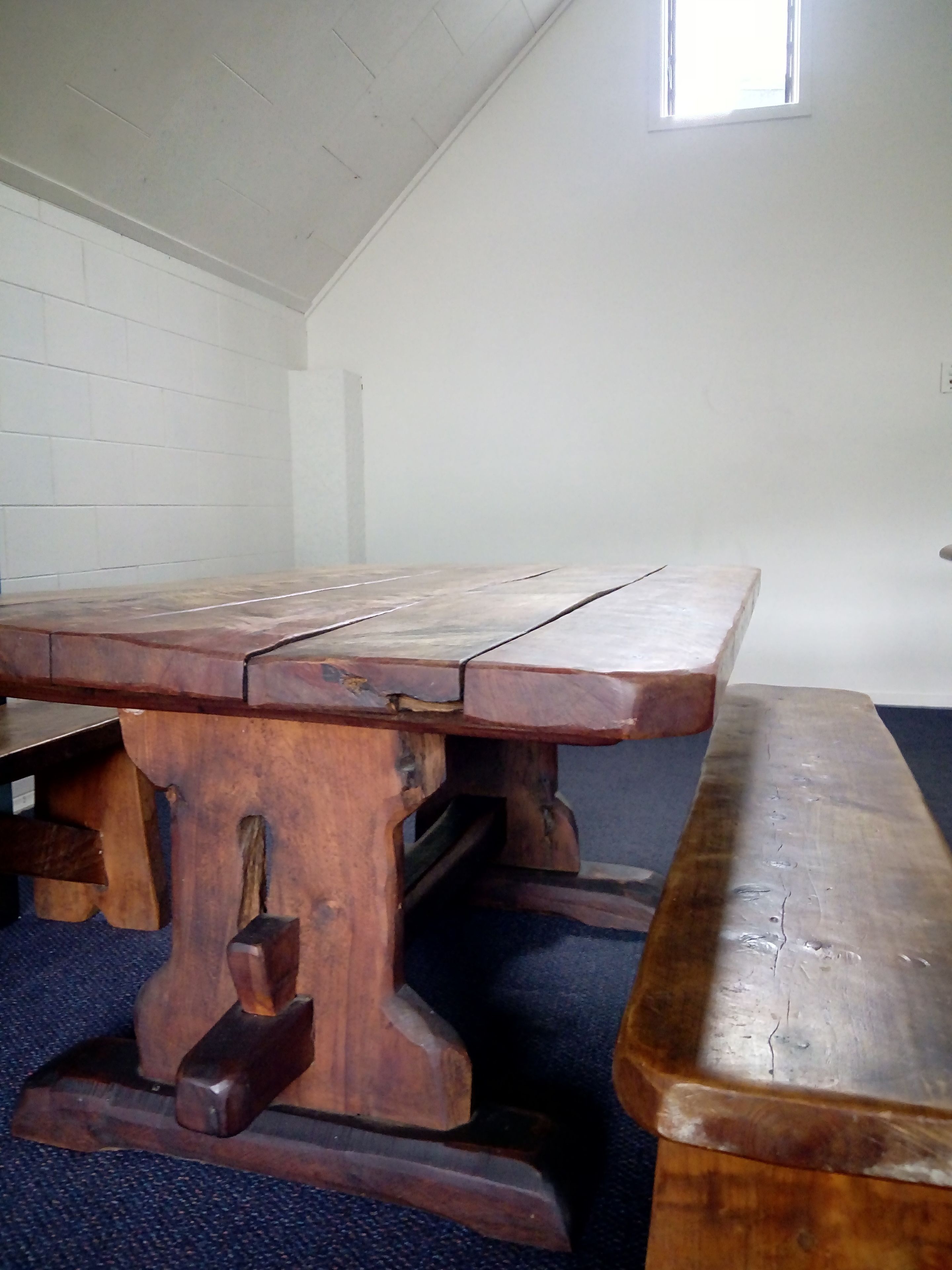 Una mesa de madera con un banco en una habitación de paredes blancas y techo inclinado.