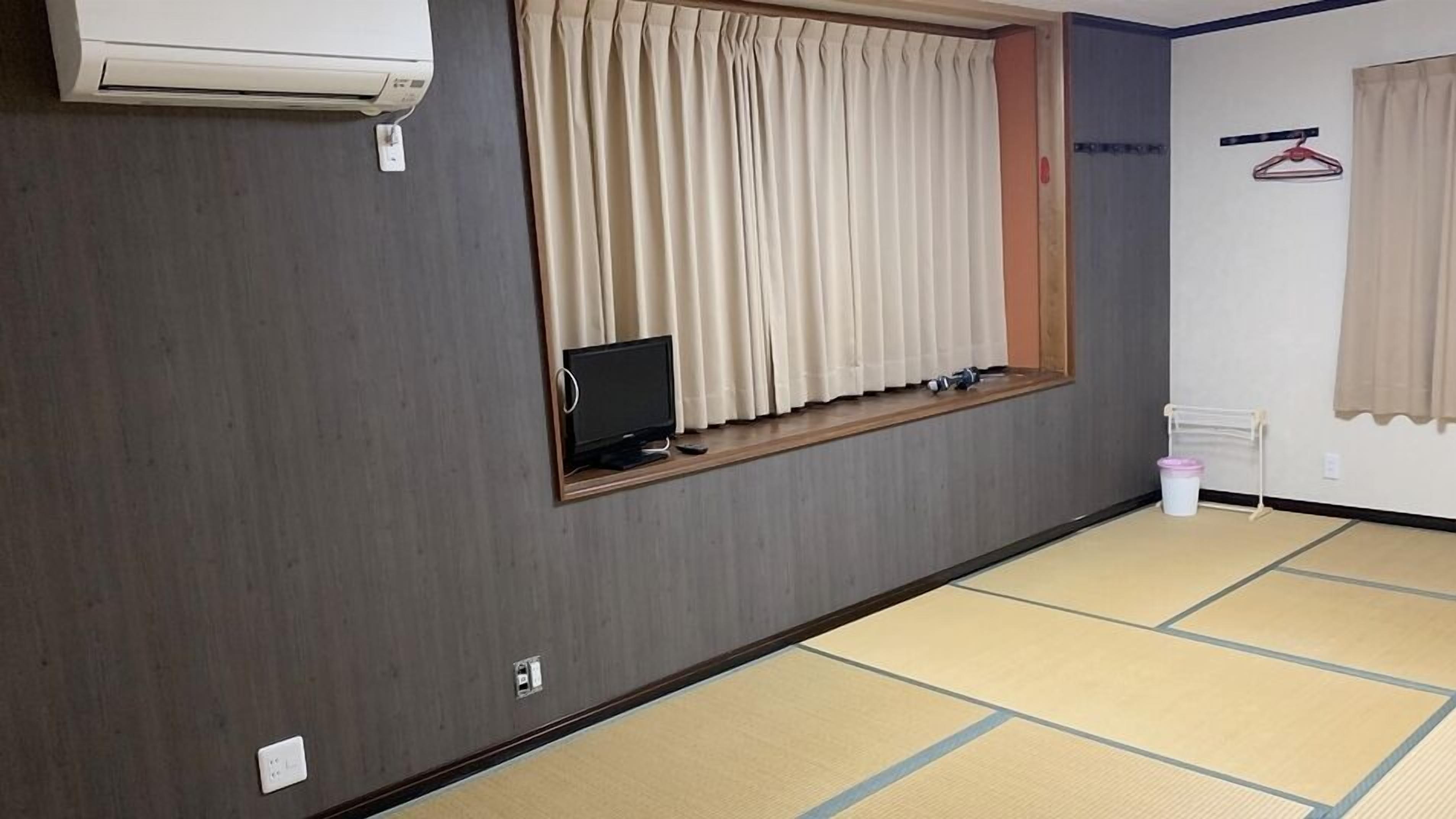 Habitació amb sòl de tatami, finestra amb cortines, televisió penjada a la paret i aire condicionat fixat a la paret.