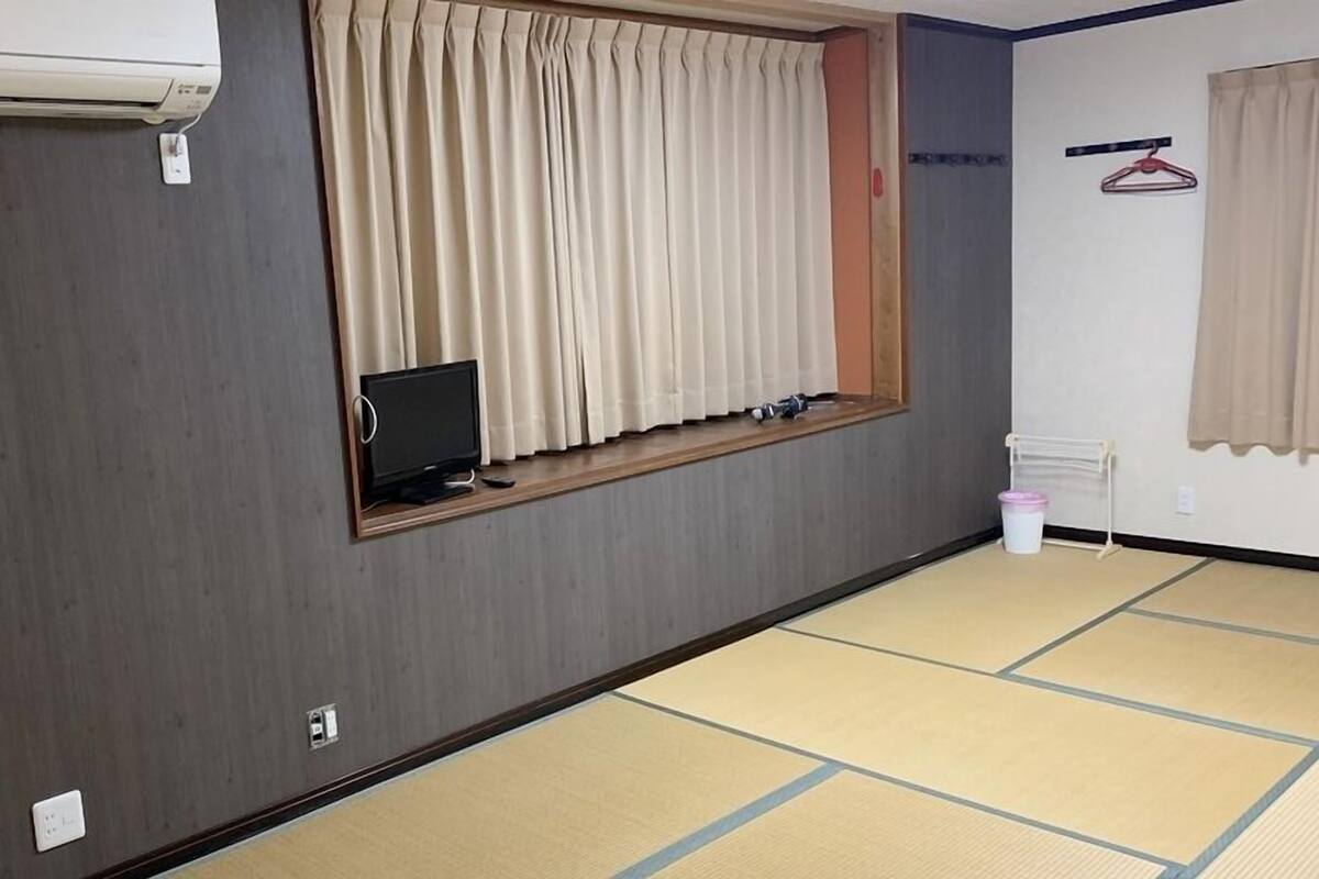 A room with tatami flooring, a window with curtains, a mounted TV, and a wall-mounted air conditioner.