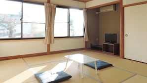 A traditional Japanese room with tatami flooring, a low table, cushions, a television, and a sliding door.