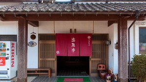 A traditional Japanese building entrance with a red banner, a vending machine, and a green mat.
