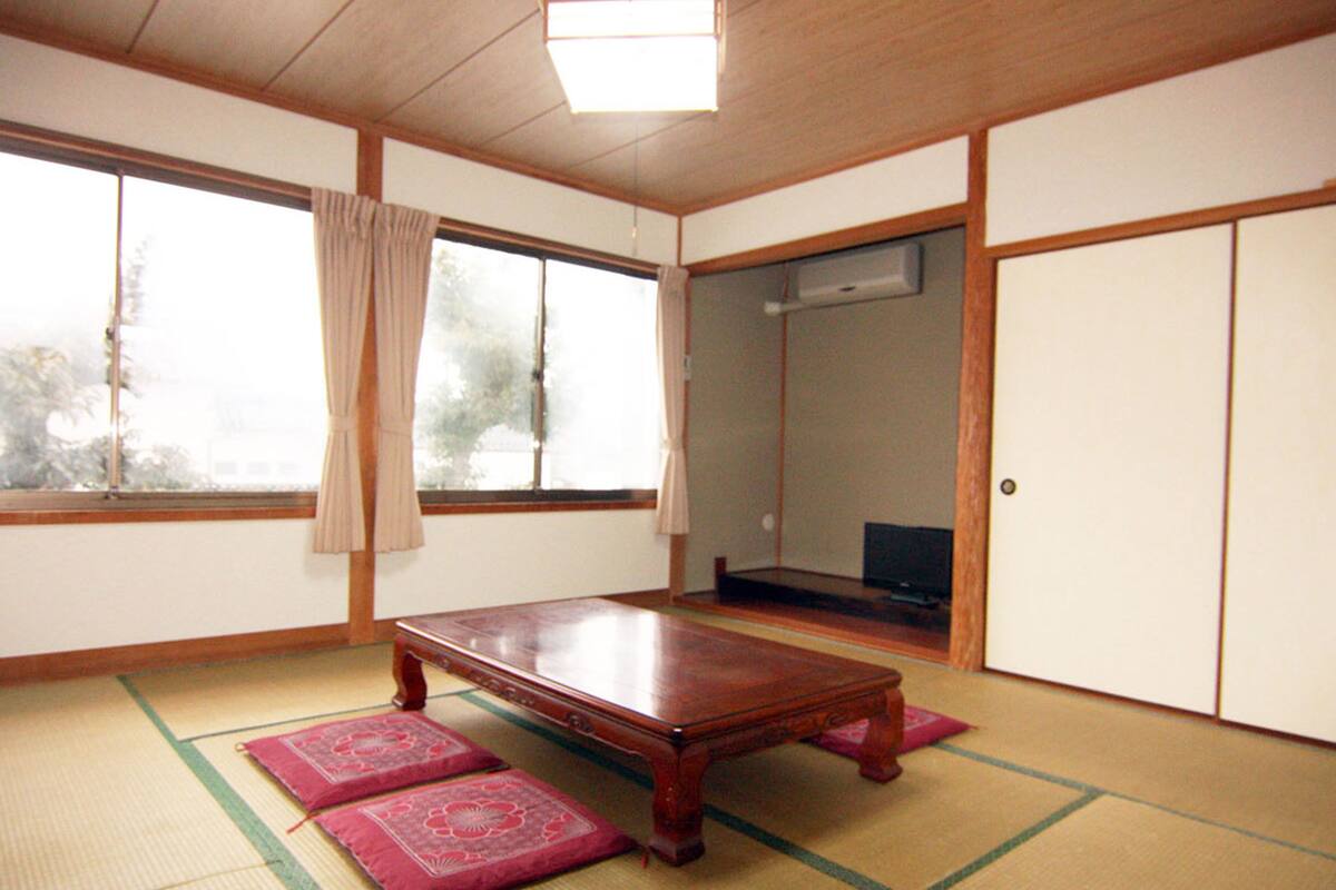 A traditional Japanese room with tatami flooring, a low wooden table, sliding doors, and a large window with curtains.