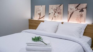 A neatly made bed with white linens and pillows, a small green plant on the bed, and three wall-mounted paintings of flowers. - VILLA23 Residence (Bangkok)