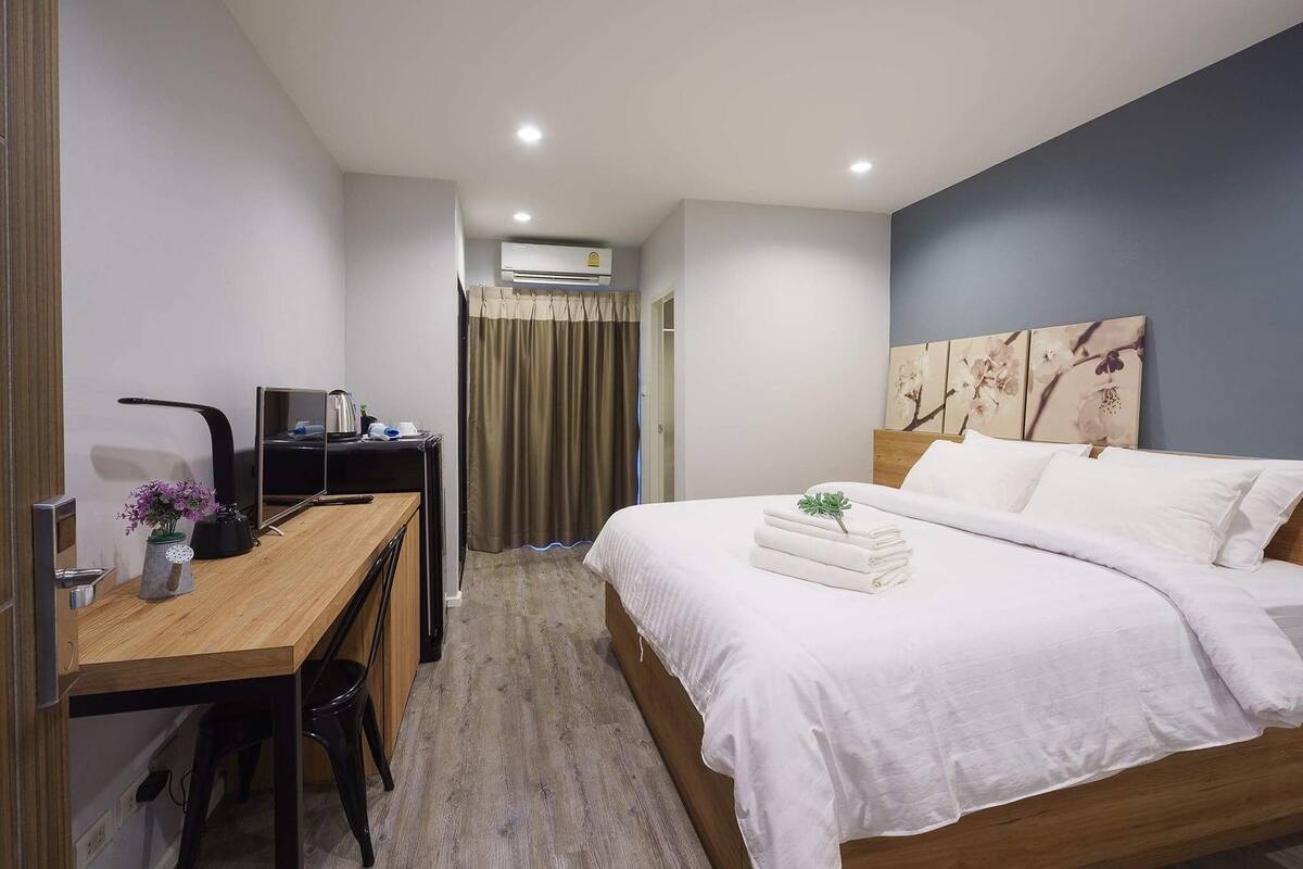 A hotel room with a wooden desk, a bed with white linens, and a large floral artwork on the wall.