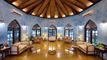 A spacious room with a high wooden ceiling, arched windows, and a central seating area with sofas and lamps.