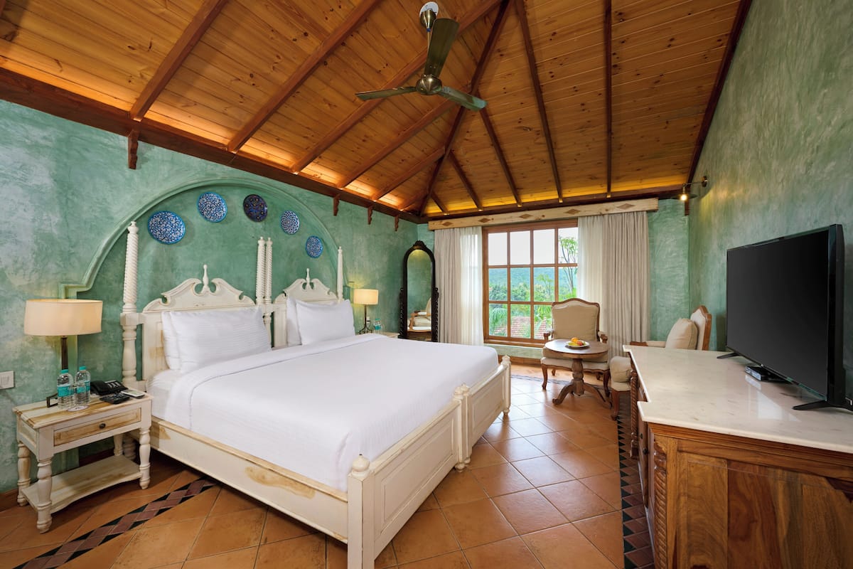 Een hotelkamer met een houten plafond, een bed, een bureau met een televisie en uitzicht op de omgeving.