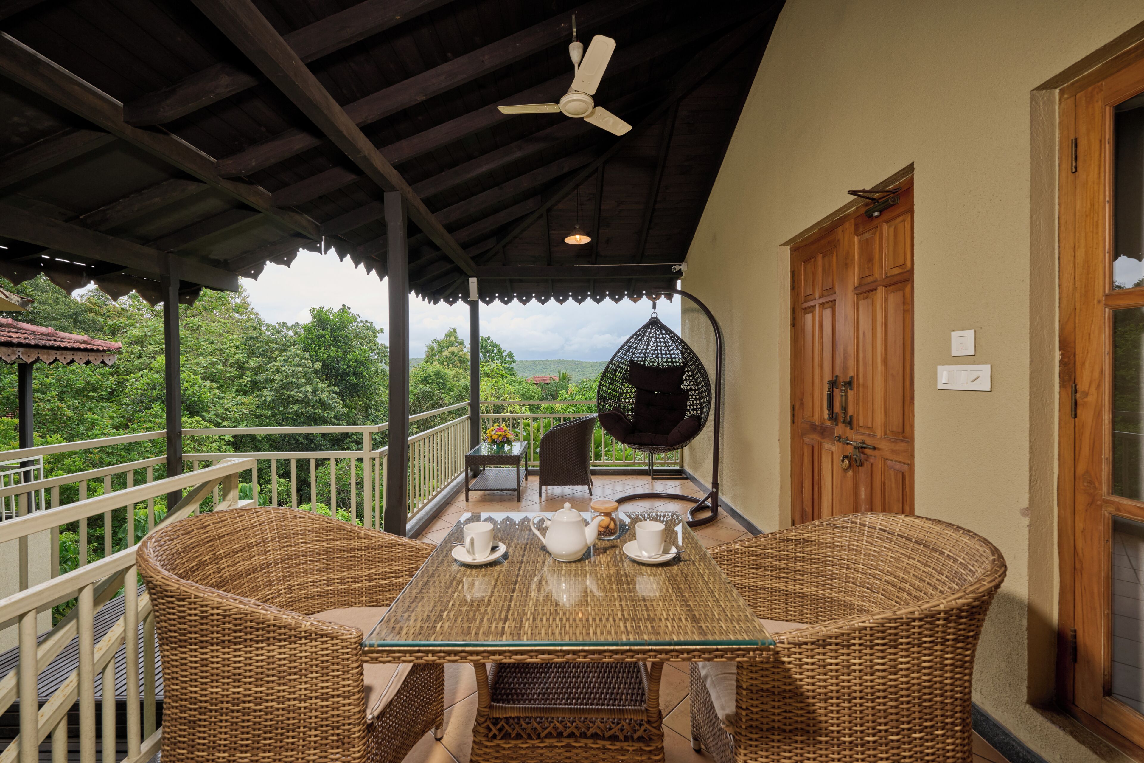 Ein überdachter Balkon mit Korbmöbeln, einem für Tee gedecktem Tisch und Blick auf Grünflächen.