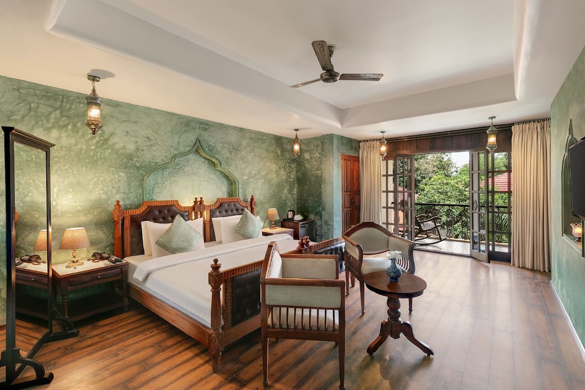 Een ruime slaapkamer met een groot bed, houten meubels, een plafondventilator en een balkon met uitzicht.