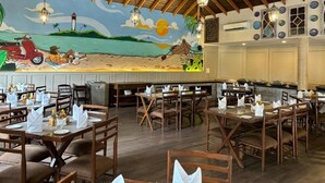Un restaurante con mesas y sillas de madera, un mural en la pared y luces colgantes.