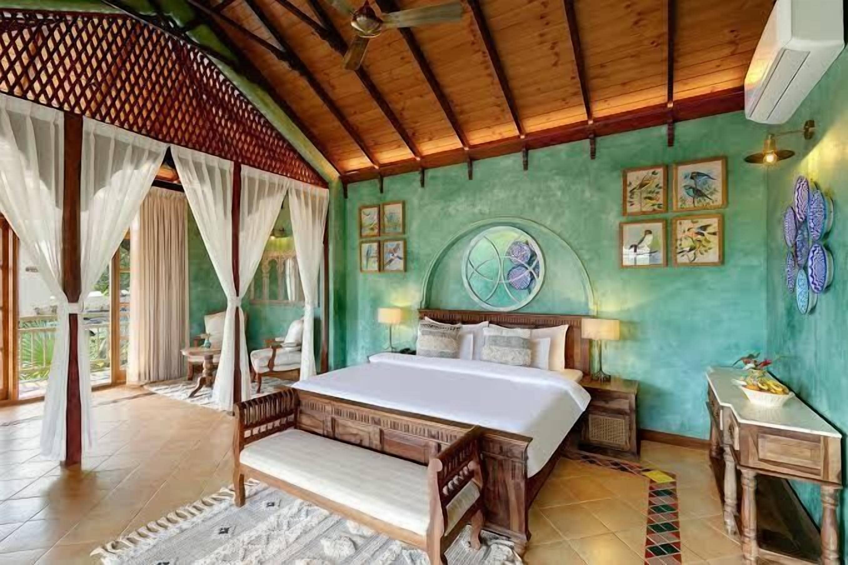 A bedroom with a bed, a ceiling fan, a window with curtains, and a wall with framed pictures.