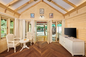 Una habitación con vigas de madera, un televisor, un armario blanco y una zona de comedor con mesa y sillas.