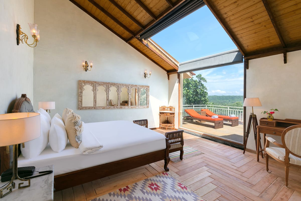 Een slaapkamer met een groot bed, een houten bureau, een stoel, en een balkon met uitzicht.