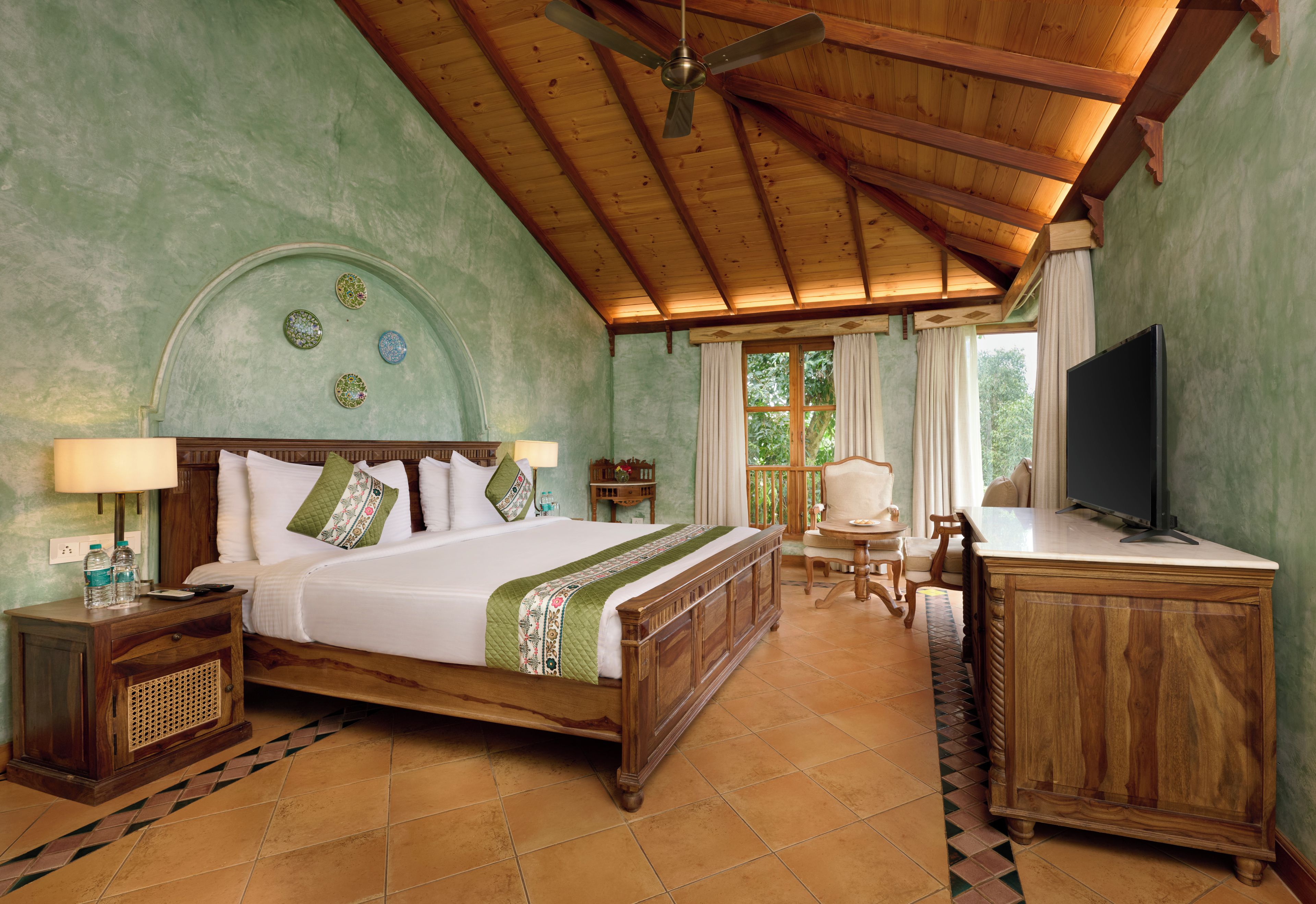 A hotel room with a wooden bed, a desk, a television, and a ceiling fan.
