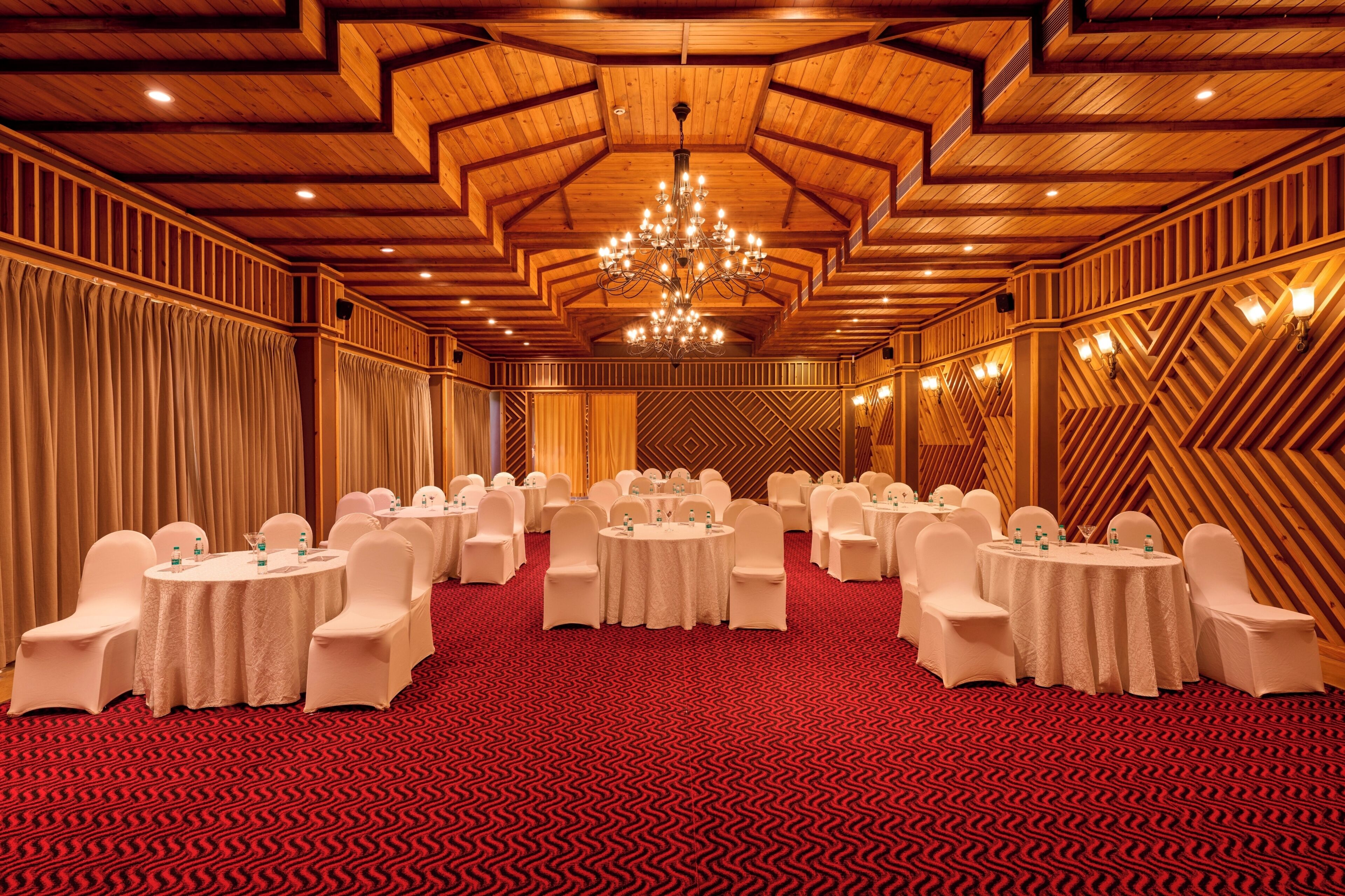A conference room with round tables, white chairs, and a red patterned carpet.