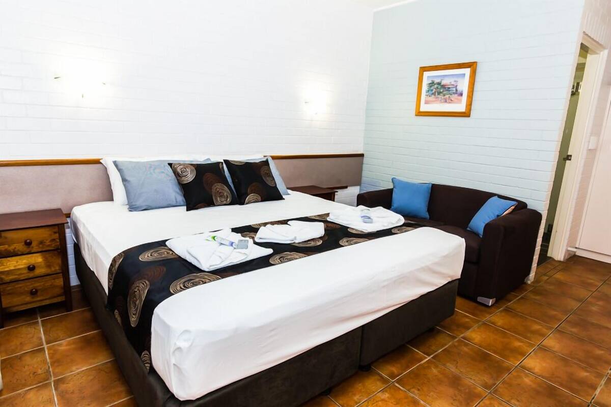 A hotel room with a bed, a sofa, a wooden nightstand, and a framed picture on the wall.