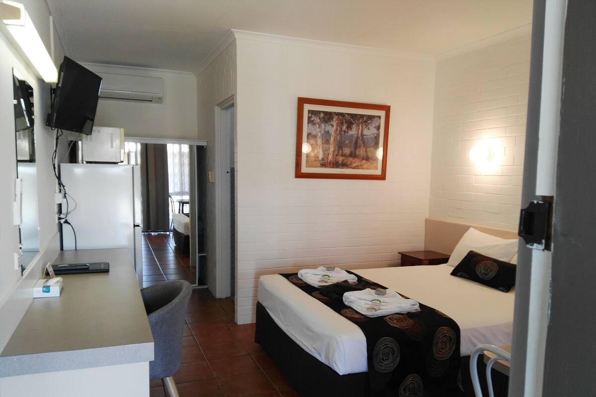 A hotel room with a bed, a desk, a chair, a TV, and a painting on the wall.