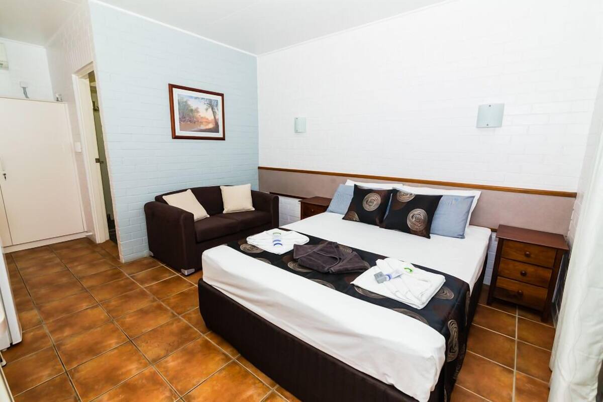 A hotel room with a bed, a sofa, a nightstand, and a picture on the wall.