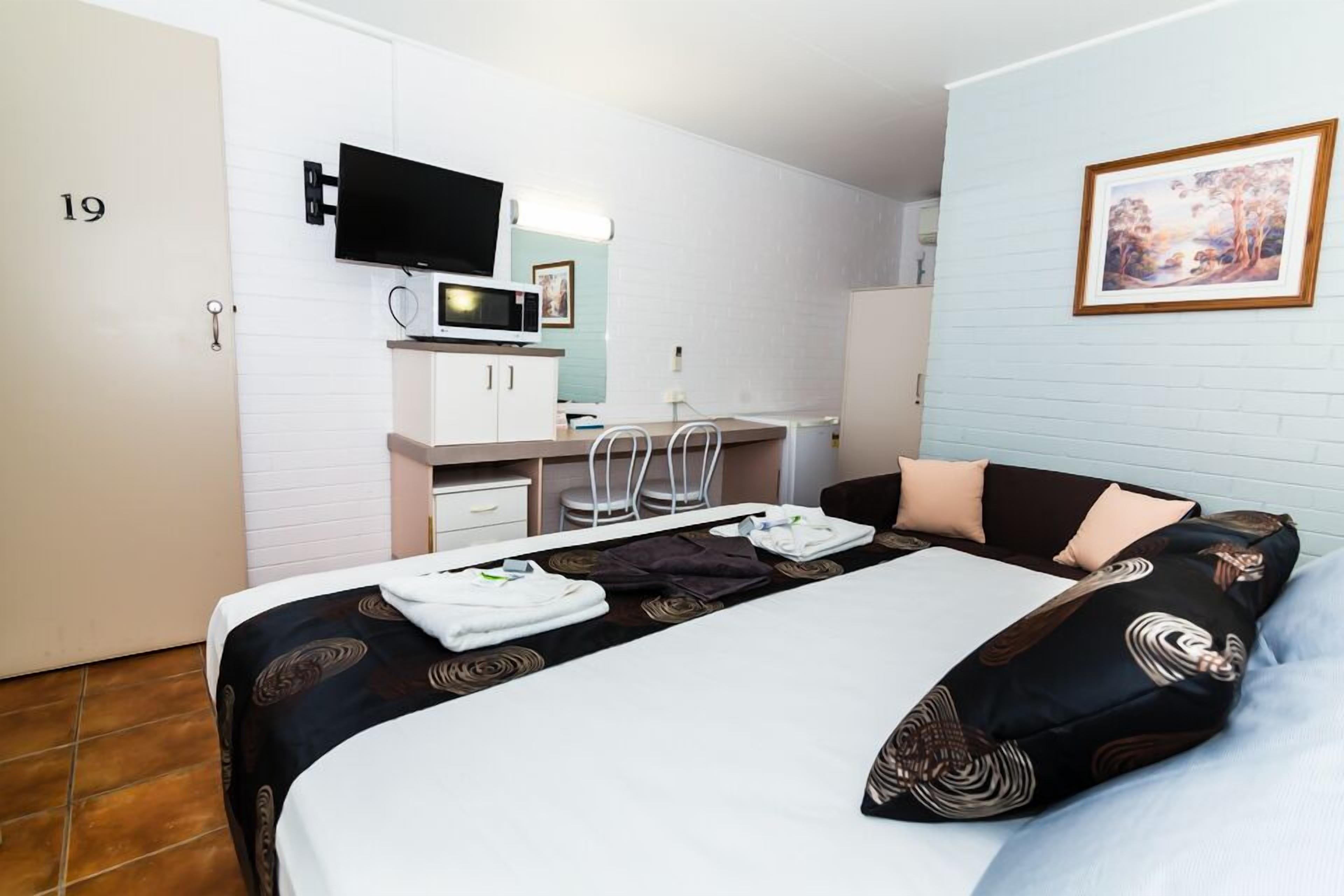 A hotel room with a bed, a desk with a computer and a flat-screen TV, a bathroom, and a framed picture on the wall.