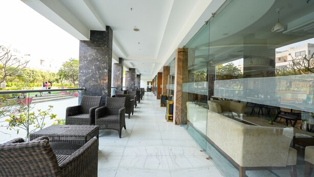 A covered outdoor seating area with wicker furniture, marble pillars, and a glass partition. - Mystical Valley View Resort and Spa, Udaipur (Udaipur)
