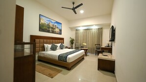 A hotel room with a large bed, a ceiling fan, a television, a desk, and a window with curtains. - Mystical Valley View Resort and Spa, Udaipur (Udaipur)