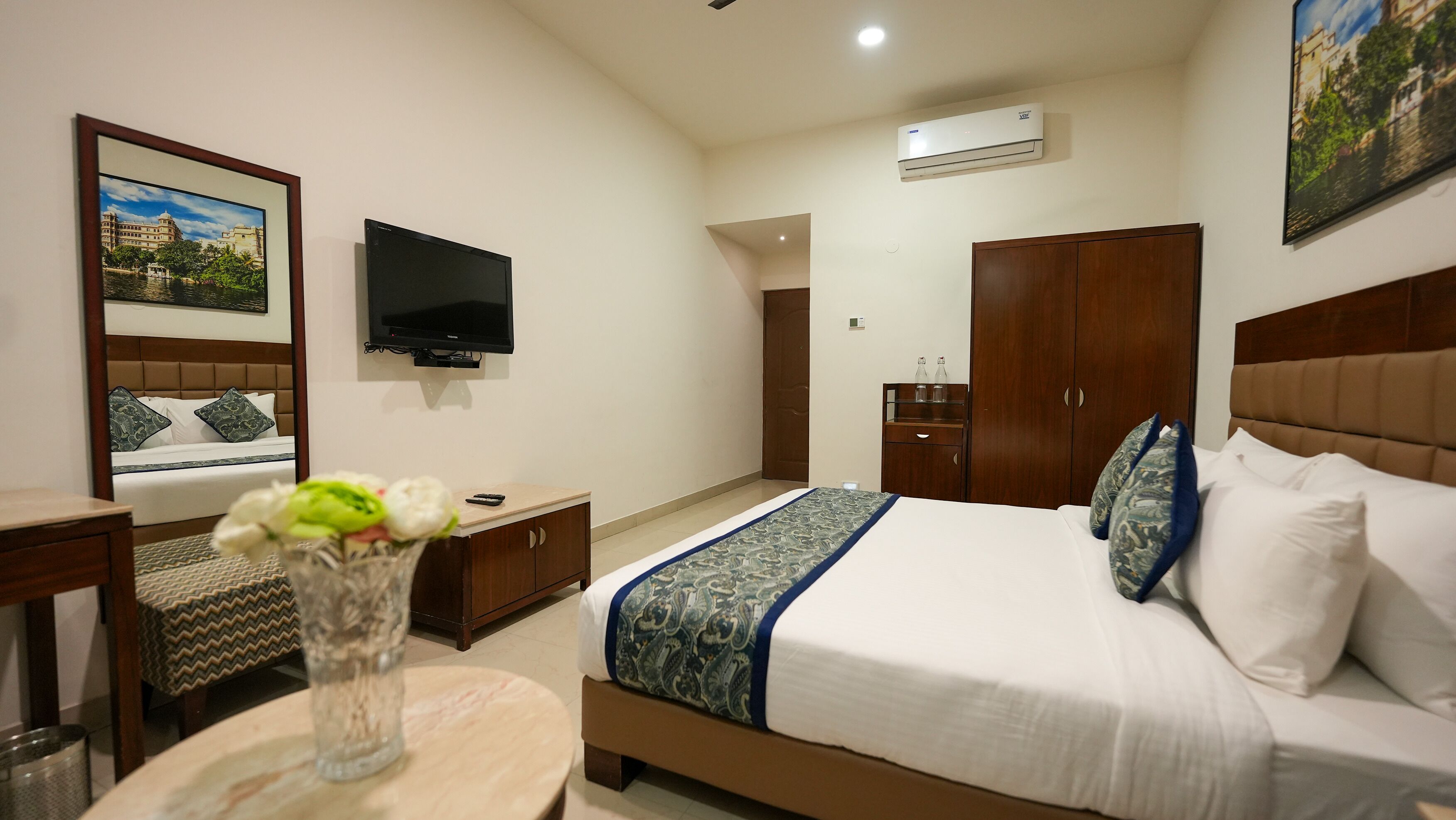 Habitación de hotel con cama, televisión, escritorio, armario y un cuadro en la pared.