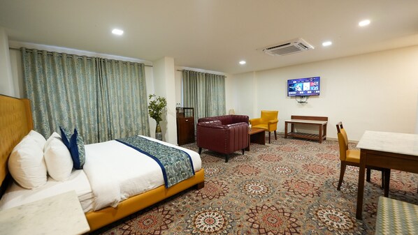 A hotel room with a bed, a desk, a chair, a television, and a patterned carpet.