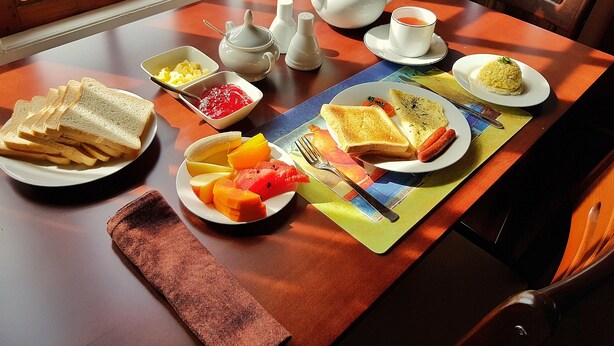 Een ontbijttafel met borden vol toast, worstjes, fruit en een theepot.