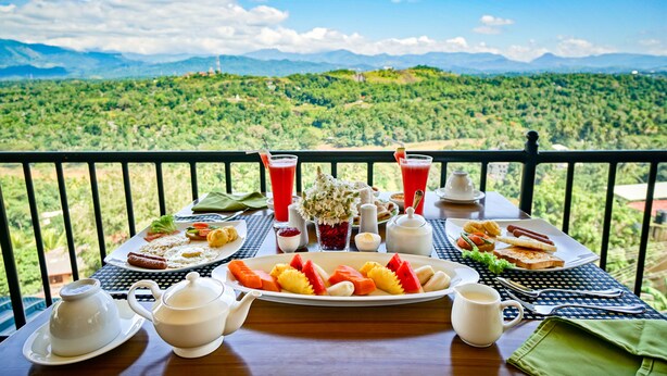 A breakfast table with a variety of food items and drinks, set against a scenic mountain backdrop. - Romance Hills Hotel (Kandy)
