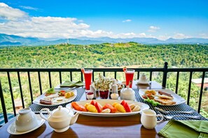 Une table de petit-déjeuner dressée avec une variété d’aliments et de boissons, le tout mis en valeur par un paysage montagneux pittoresque en arrière-plan.