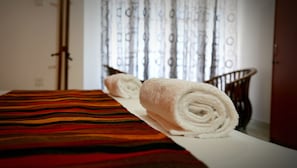 A neatly made bed with a striped bedspread and two rolled towels. - Romance Hills Hotel (Kandy)