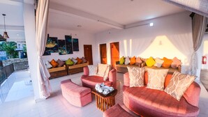 A spacious living area with a red sofa set, a coffee table, and a wooden side table. There are multiple colorful cushions on the sofas. - Romance Hills Hotel (Kandy)