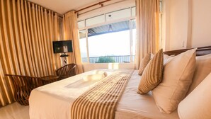 A hotel room with a bed, a desk, a chair, a TV, and a window with a view. - Romance Hills Hotel (Kandy)