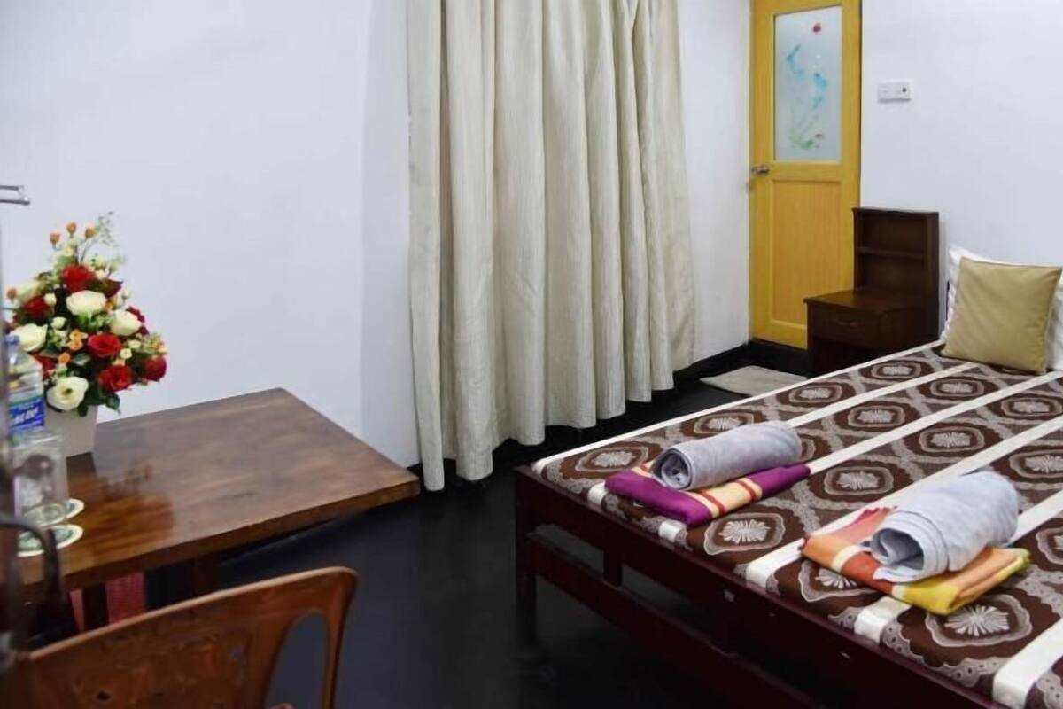 A small hotel room with a bed, a desk, a chair, and a vase of flowers.