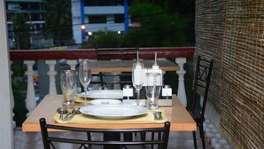 A dining table set with plates, cutlery, glasses, and a salt and pepper shaker on a balcony with a view of buildings and greenery. - Lodge in 611 (Kandy)