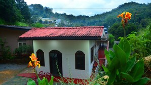 A small building with a red roof and arched windows, surrounded by greenery and a hilly landscape. - Lodge in 611 (Kandy)