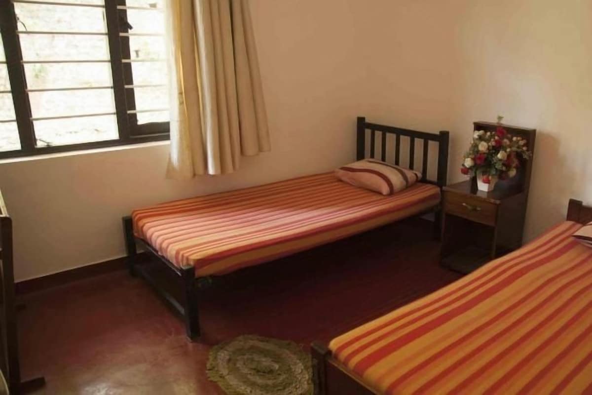 A room with two single beds, a small table with a vase of flowers, and a window with curtains.