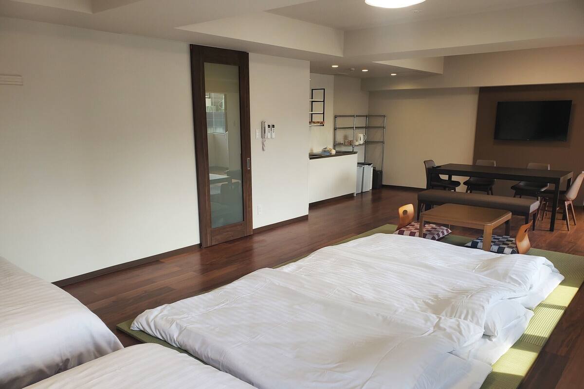 A hotel room with two beds, a dining area, a TV, and a kitchenette.